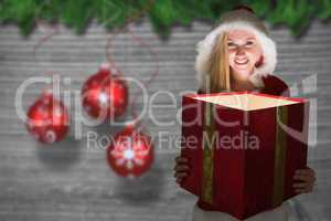 Composite image of festive blonde looking into glowing gift