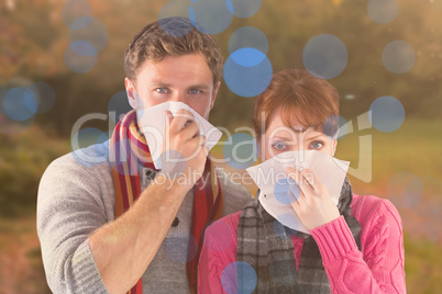 Composite image of couple blowing noses into tissues