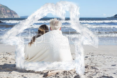Composite image of couple sitting on the beach under blanket loo