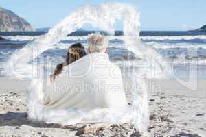 Composite image of couple sitting on the beach under blanket loo