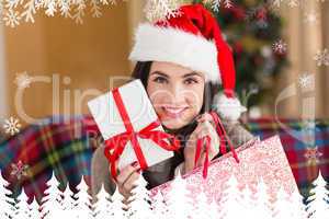 Composite image of smiling brunette holding gift and shopping ba