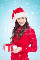 Composite image of smiling brunette in santa hat holding a gift