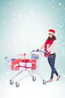 Composite image of brunette in santa hat with shopping trolley