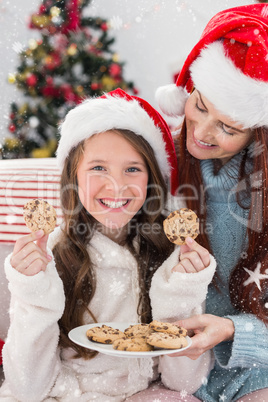 Composite image of festive mother and daughter on the couch with cookies