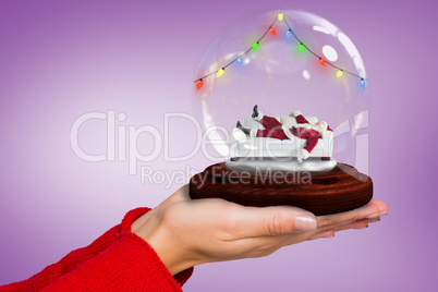 Composite image of hand holding santa snow globe