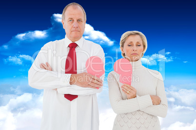 Composite image of older couple standing holding broken pink hea