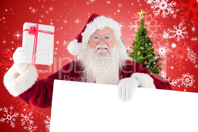 Composite image of santa shows a present while holding sign