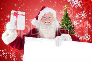 Composite image of santa shows a present while holding sign