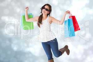Composite image of happy brunette with sunglasses holding shoppi