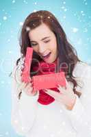 Composite image of surprised brunette opening christmas gift