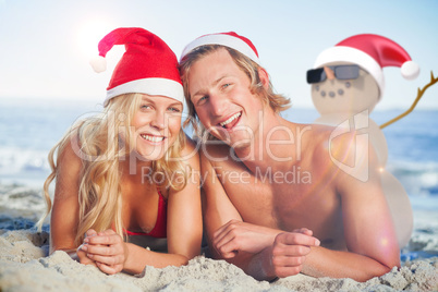 Composite image of couple lying on beach wearing christmas hats