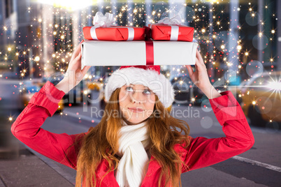 Composite image of festive redhead holding pile of gifts