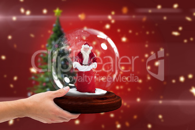 Composite image of hand holding snow globe