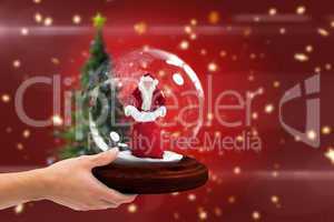 Composite image of hand holding snow globe