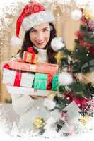 Composite image of festive brunette holding pile of gifts near a christmas tree