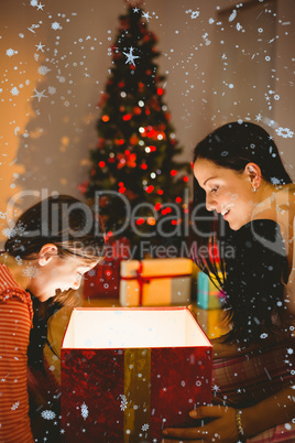 Composite image of festive mother and daughter opening a glowing christmas gift