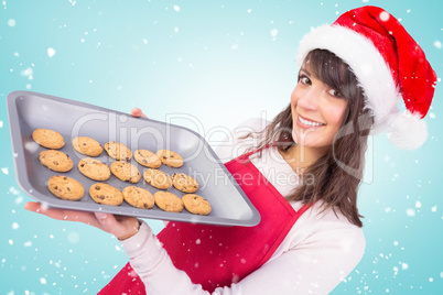 Composite image of brunette in santa hat offering hot cookies