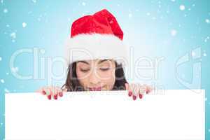 Composite image of pretty brunette in santa hat showing white po