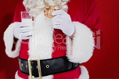 Composite image of santa holding cookie and glass of milk