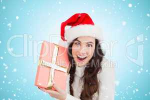 Composite image of festive brunette holding gift