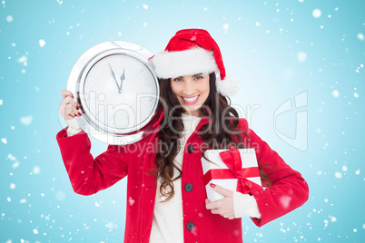 Composite image of festive brunette holding a clock and gift