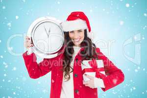 Composite image of festive brunette holding a clock and gift