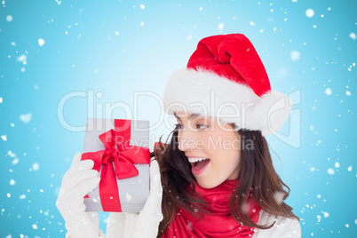 Composite image of astonished brunette in santa hat showing gift