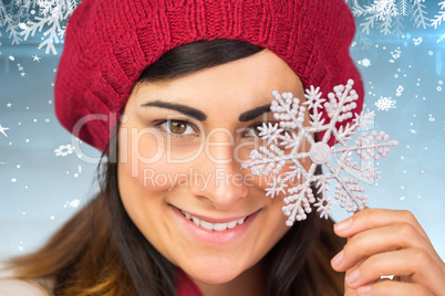 Composite image of smiling brunette in hat holding snowflake