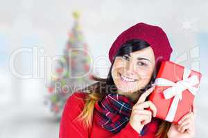 Composite image of smiling brunette in red hat holding gift