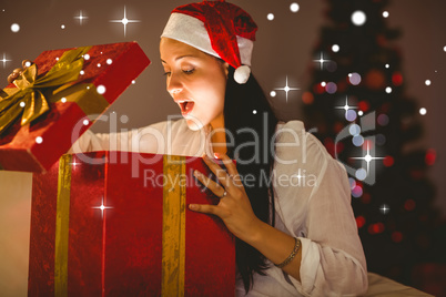 Composite image of festive brunette opening a glowing christmas