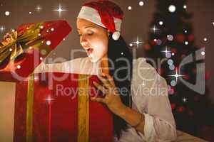 Composite image of festive brunette opening a glowing christmas