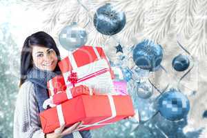 Composite image of smiling brunette holding pile of gifts