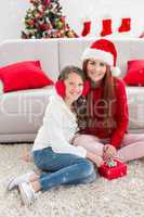 Composite image of festive mother and daughter opening a christmas gift
