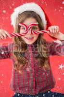 Composite image of happy little girl in santa hat holding candy canes
