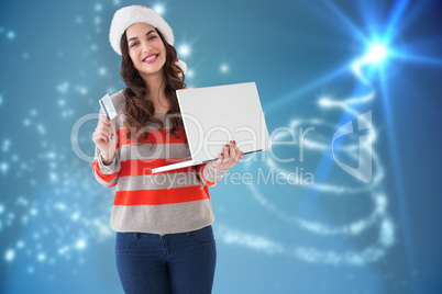 Composite image of festive brunette holding laptop and credit ca