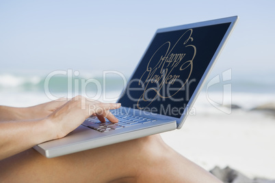 Composite image of woman sitting on beach using her laptop