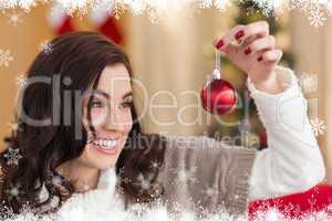 Composite image of smiling brunette holding a bauble at christma