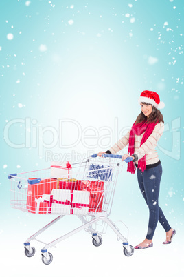 Composite image of brunette in santa hat with shopping trolley