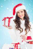 Composite image of cheerful brunette in santa hat holding gift