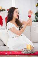 Composite image of smiling brunette holding a bauble at christmas