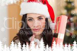 Composite image of pretty brunette holding gift at christmas