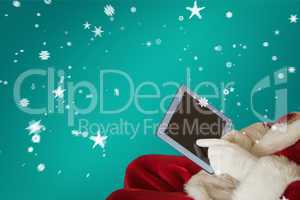 Composite image of santa using tablet on the armchair