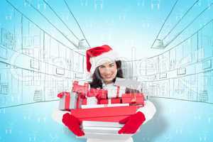 Composite image of smiling brunette in santa hat holding stack o