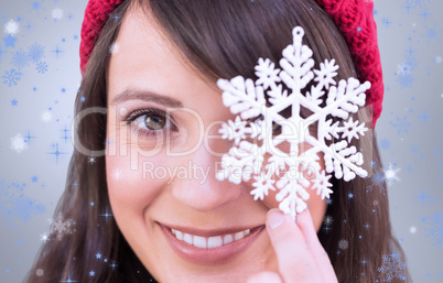 Composite image of festive brunette holding snowflake decoration