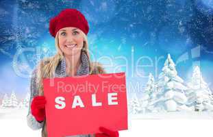 Composite image of blonde in winter clothes holding sale sign