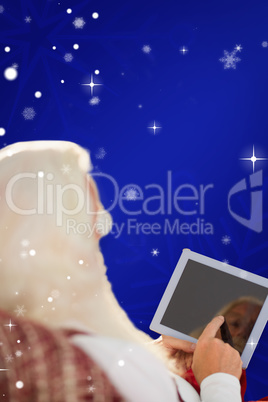 Composite image of rear view of santa using tablet on the armcha