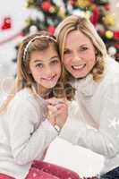 Composite image of festive mother and daughter beside christmas tree