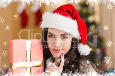 Composite image of pretty brunette holding gift at christmas