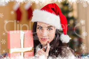 Composite image of pretty brunette holding gift at christmas
