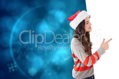 Composite image of smiling brunette in santa hat pointing white